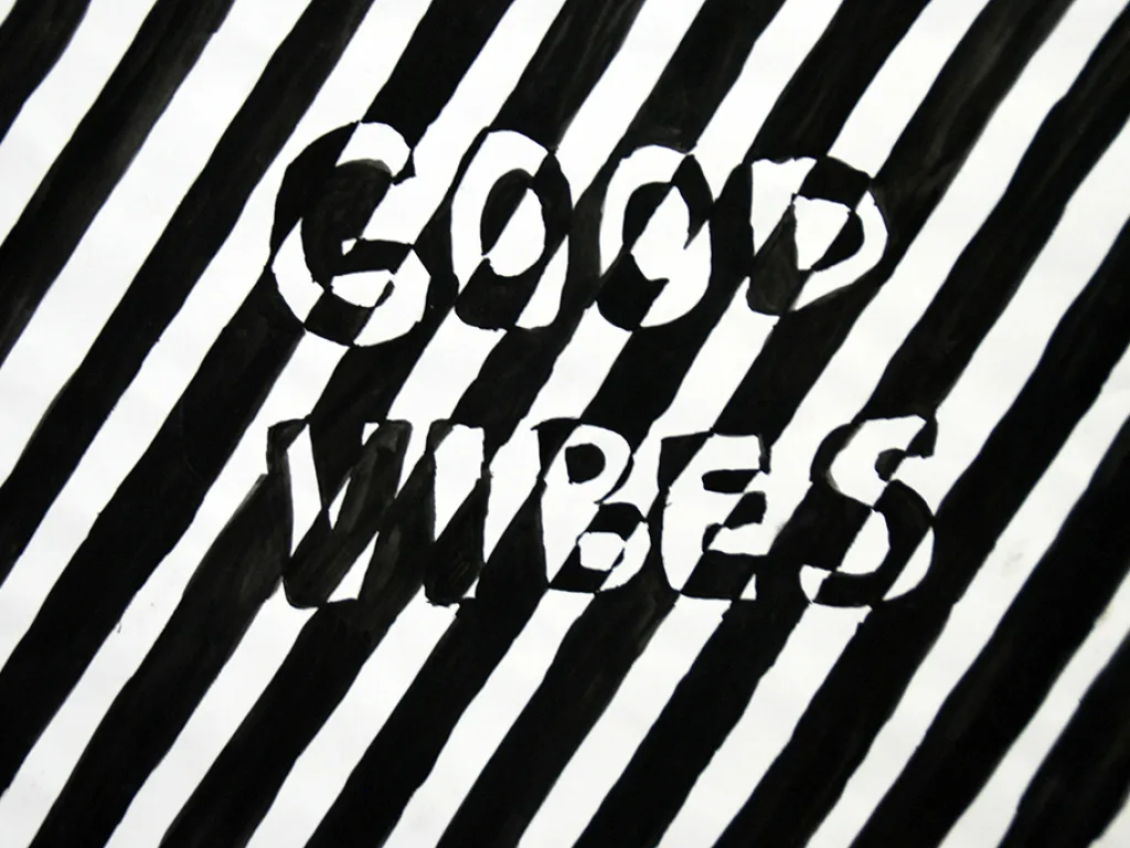 Ein Schriftzug „Good Vibes“ als Scherenschnitt auf schwarz-weiß gestreiftem Grund.